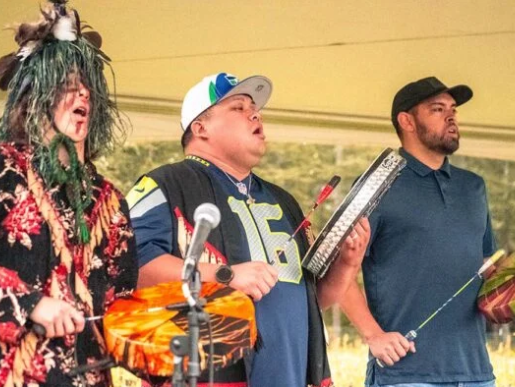 Three performers hold drums and sing while standing onstage at Family Tides Fall Fest
